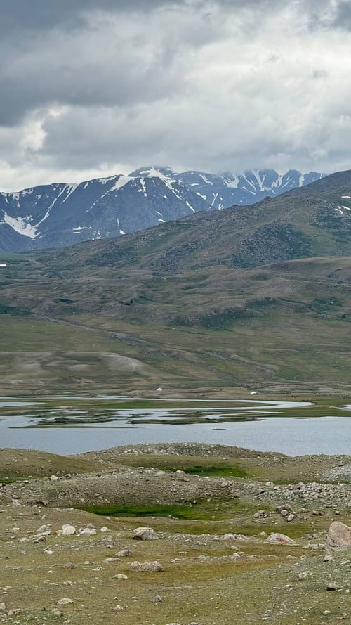 An alpine lake framed by snow-capped mountains with distant gers