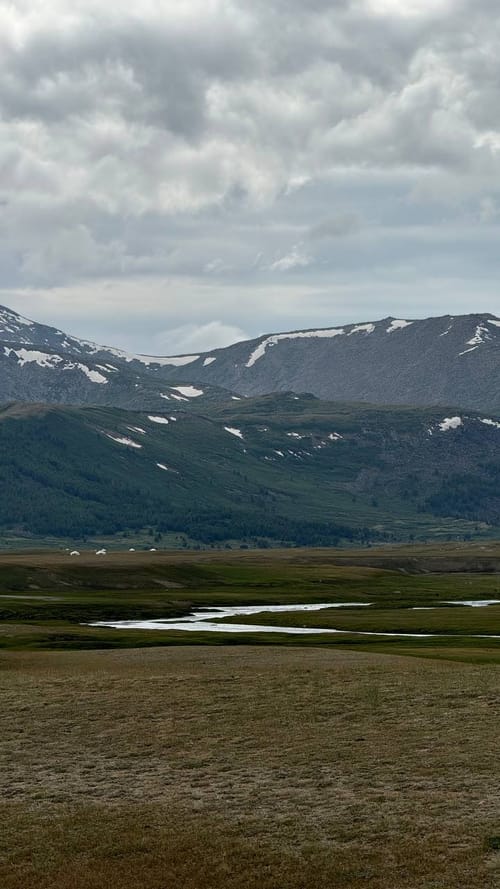 A river winding through a green valley beneath snow-streaked peaks